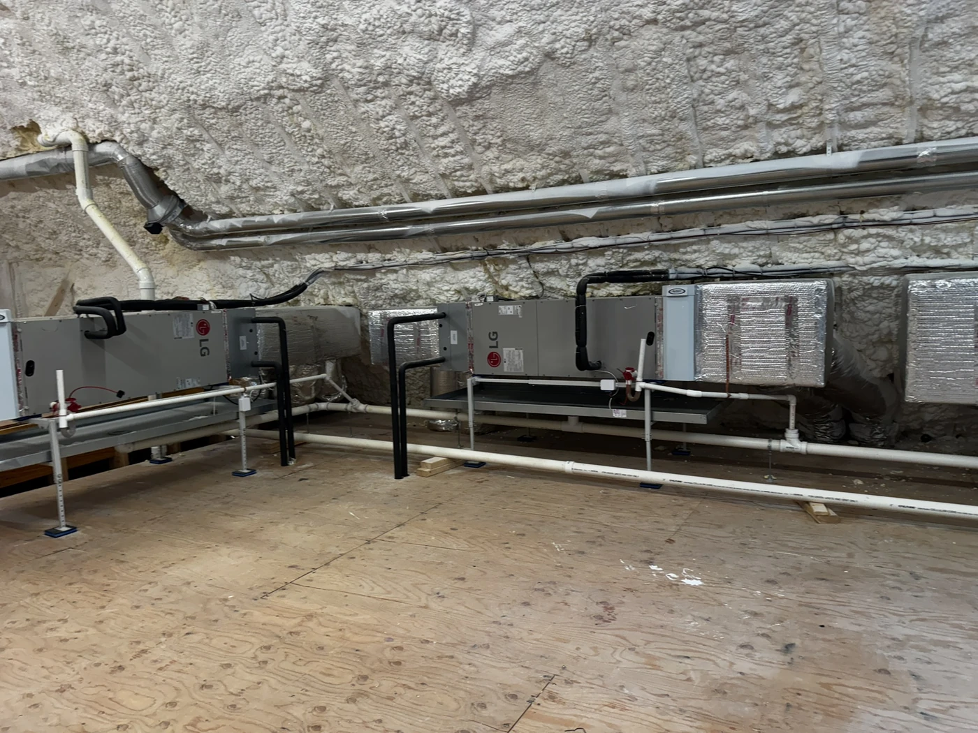Two horizontal air handlers on raised stands in an insulated attic