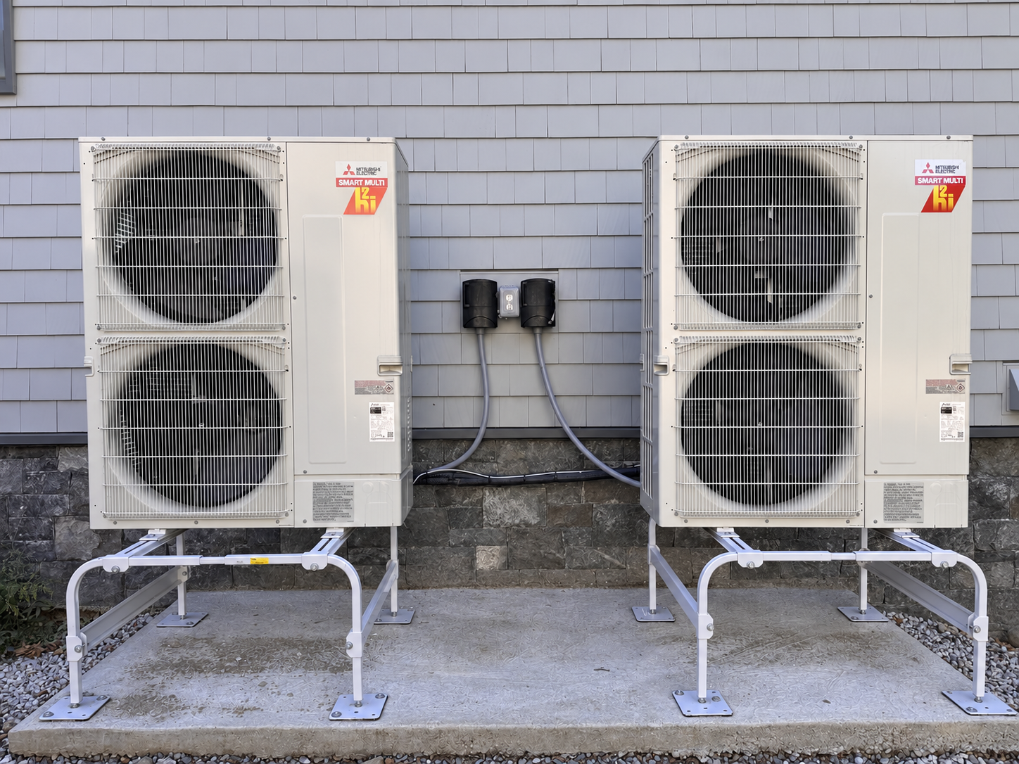 Two Mitsubishi double-fan outdoor heat pump units on raised stands